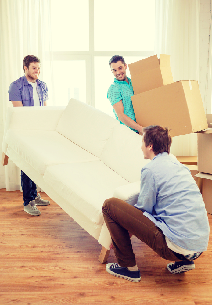 moving, real estate and friendship concept - smiling male friends with sofa and boxes at new home